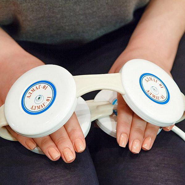 A Close-Up Of A Person Holding The Almagia International ALMAG-01 PEMF Therapy Device Over Their Hands And Lap