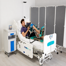 A Man Lying On A Hospital Bed Reading A Book While Using The Kinetec Spectra Essential Knee CPM Machine Which Is Used For Knee Rehabilitation
