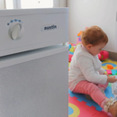 A Sandstone Austin Air Systems HealthMate Plus Standard Air Purifier In The Foreground, With A Baby Sitting On A Colorful Play Mat In The Background