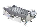 An Adjustable Hospital Bed With The Wellell Optima Turn Lateral Rotation Pressure Relief Mattress With Stretch Cover On It, White Side Rails, And A Digital Control Unit On The Footboard
