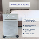Austin Air Systems Bedroom Machine Air Purifier Shown In The Sandstone Labeled 'The Bedroom Machine' Shown In A Bedroom Setting Next To A Bed. Text On The Right Lists Included Components: A Military-Grade HEGA Carbon Cloth, 60 sq. 