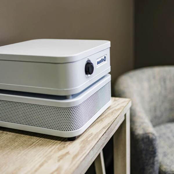 Austin Air Systems "it" Personal Compact Air Purifier On A Wooden Table With A Blurred Chair In The Background