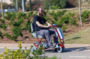 Close Up View Of A Man Riding The Tzora Feather Ultra Lightweight Mobility Scooter Shown In The Red Color During The Day