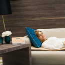 Close Up View Of A Woman Resting On The Cellvital Homecare CV-HC PEMF Therapy System Mat Shown On A Couch With The Control Unit Seen On The Edge Of A Table
