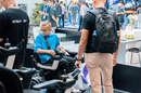Close Up View Of A Young Boy Sitting In The STRUTT ev1 Smart Electric Mobility Vehicle With Several People Around Shown In A Convention Center Setting