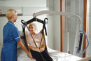 Close Up View Of An Elderly Woman In A Sling Being Carried By The Joerns Hoyer® Presence Pro HD Patient Lift With A Healthcare Worker Assisting Her In A Hospital Room Setting