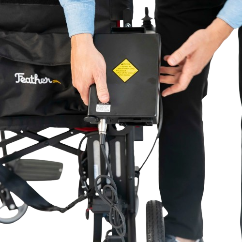 Close Up View Of The Feather Electric Wheelchair Shown With Person Holding The Battery