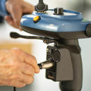 Close Up View Of The Journey So Lite Mobility Scooter Charging Port On The Tiller Shown In Blue Color With Hands Attaching The Cable And Holding The Handle
