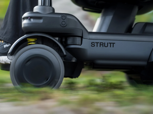 Close Up View Of The Lower Portion Of The STRUTT ev1 Smart Electric Mobility Vehicle Shown In Motion On A Grassy Terrain