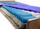 Close Up View Of The Proactive Medical Protekt Aire 9900 Low Air Loss/Alternating Mattress System Shown With The Top Cover Removed, Revealing Multiple Blue Air Chambers And A Gray Fabric Liner, With A Purple Quilted Mattress Topper