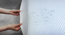 Vista de cerca del protector de colchón impermeable para la cama giratoria StarSleep Arlo con unas manos estirándolo y gotas de agua sobre su superficie
