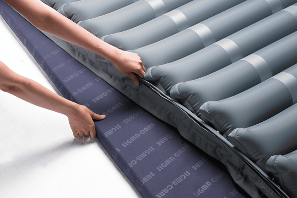 Close Up View Of The Wellell Domus 3 Alternating Pressure Redistribution Mattress System With Quilted Cover Shown With Two Hands Adjusting The Mattress