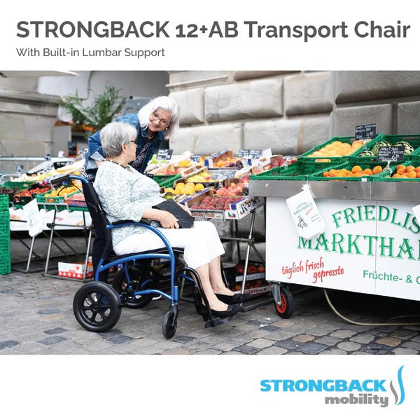 Elderly Woman Sitting In The Strongback 12 +AB Lightweight Transport Chair With Friend Standing Beside Her Shown In An Outdoor Grocery Store Environment