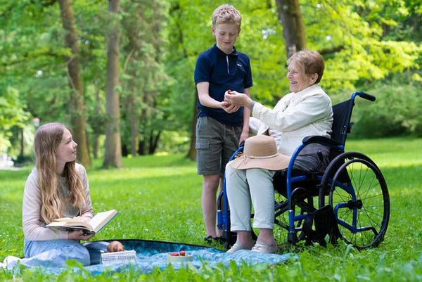 Elderly Woman Sitting In The Strongback 24 Ultra-Lightweight Wheelchair With Two Children In A Park Setting