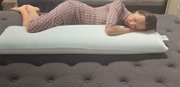 Front Centered View Of A Woman Wearing A Dress Lying On The Standard Body Eurolux Green Planet Pillow Shown In A Showroom Setting