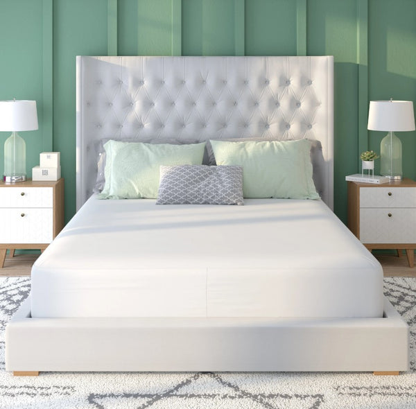 Front Centered View Of The Rize Home Smooth Mattress Protector Shown On A Bedframe In A Bedroom Featuring A Tufted Headboard Two Nightstands And Lamps Against A Green Paneled Wall