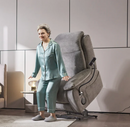 Front Left Side View Of An Elderly Woman Rising Out Of The StarSleep Starise Massage Lift Chair Shown In The Lifted Position In A Bedroom Setting