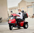 Front Left Side View Of The AFIKIM Afiscooter S3 Scooter In The Red Color With Optional Rear Lock Box Shown With An Elderly Woman Riding In A City Setting