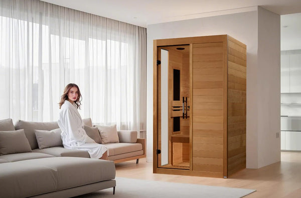 Front Left Side View Of The Dynamic Lucca 2 Person Ultra Low EMF FAR Infrared Indoor Sauna | DYN-6215-05 Elite Shown With A Woman Sitting On A Couch Next To The Sauna In An Indoor Setting