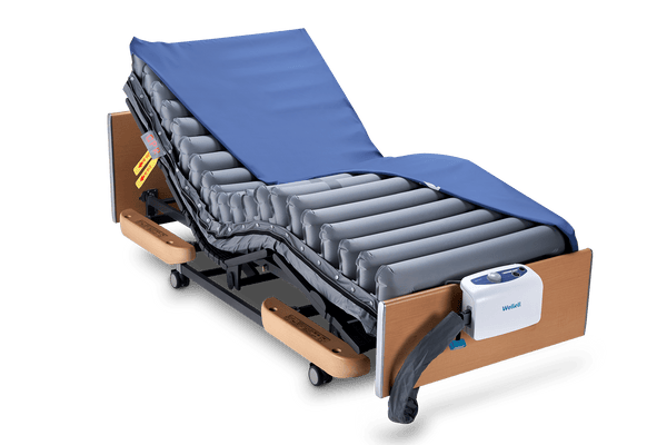 Front Left Side View Of The Wellell Domus 3 Alternating Pressure Redistribution Mattress System With Quilted Cover Shown On An Adjustable Bed With The Control Unit Hanging On The Footboard With The Cover Slightly Removed