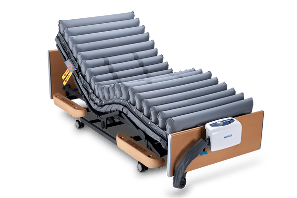 Front Left Side View Of The Wellell Domus 3 Alternating Pressure Redistribution Mattress System With Quilted Cover Shown On An Adjustable Bed With The Control Unit Hanging On The Footboard Without The Cover