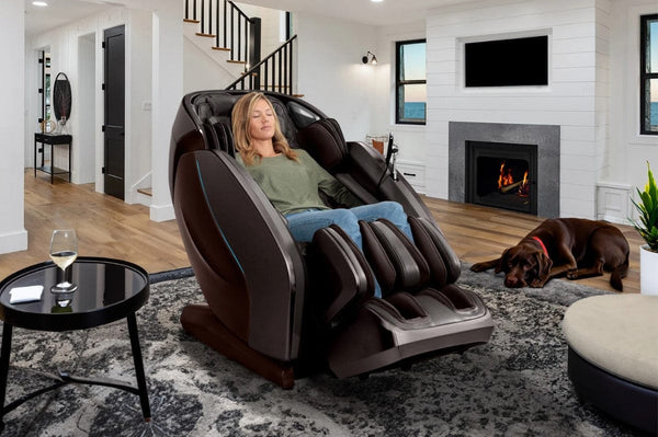 Front Right Side View Of The Kyota Hatsumei M900 AI 4D Massage Chair Shown In An Indoor Setting In Dark Brown Color With Woman Sitting In The Chair