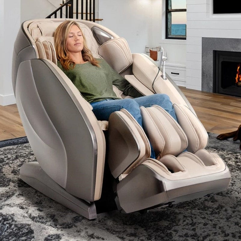 Front Right Side View Of The Kyota Hatsumei M900 AI 4D Massage Chair Shown In An Indoor Setting In Gray And Tan Color With Woman Sitting In The Chair