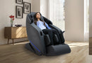 Front Right Side View Of The Kyota Yugana M780 4D Massage Chair In Black Color Shown In An Indoor Setting With A Woman Sitting In The Chair
