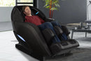 Front Right Side View Of The Kyota Yutaka M898 Massage Chair Shown In The Black Color In An Indoor Setting With A Man Sitting In The Chair