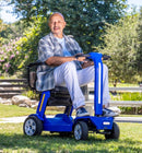 Front Right Side View Of The Reyhee Flex Electric Folding Mobility Scooter With A Blue Frame In An Outdoor Setting During The Day With An Elderly Man Driving