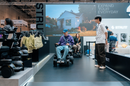 Front View Of A Man And A Woman Using The STRUTT ev1 Smart Electric Mobility Vehicle In A Convention Center Setting