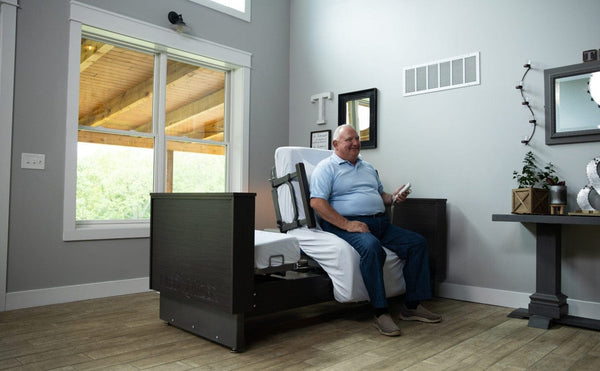 Front View Of The Med Mizer Active Care Deluxe Rotating Bed And Bed In The Chair Position In A Home Setting With An Elderly Man Sitting In The Bed Using The Remote Control
