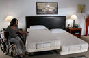 Front View Of The Transfer Master Supernal Hi Low Adjustable Bed In Split King Size With Woman In Wheelchair Using The Remote To Elevate The Bed