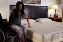 Front View Of The Transfer Master Supernal Hi Low Adjustable Bed Split King Size With A Woman In A Wheelchair Transferring Onto Bed