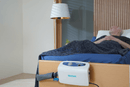 Front View Of The Wellell Domus 3 Alternating Pressure Redistribution Mattress System With Quilted Cover Shown With A Man Lying On The Mattress System In A Home Care Setting With The Control Unit Hanging On The Footboard