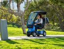 Left Side View Of The AFIKIM Afiscooter C4 Scooter Shown With Optional Hard Top Canopy In The Blue Color Seen In An Outdoor Daytime Park Setting With Trees In The Background
