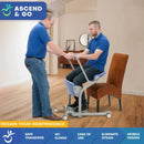 Left Side View Of The Ascend & Go Sit to Stand Patient Lift Shown With A Man Sitting In The Chair Of The Lift With A Healthcare Worker Assisting Him In A Home Care Setting