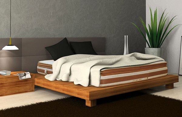 Left Side View Of The Eurolux Lux By Naturalia: The 6-Layer Luxury Mattress Crafted By Masters Shown On A Wooden Platform Bed Frame In A Bedroom Setting With A White Blanket And Two Black Pillows On The Mattress