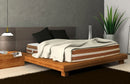 Left Side View Of The Eurolux Lux By Naturalia: The 6-Layer Luxury Mattress Crafted By Masters Shown On A Wooden Platform Bed Frame In A Bedroom Setting With A White Blanket And Two Black Pillows On The Mattress