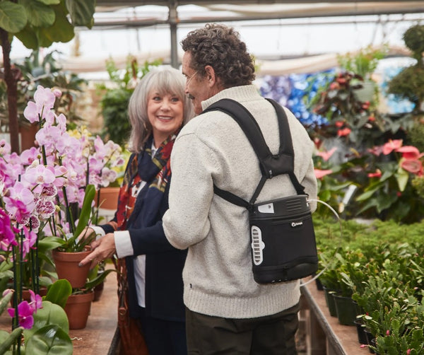 Man And Woman Shopping For Plants In A Greenhouse Shown With Man Using The O2 Concepts Oxlife Liberty2 Portable Oxygen Concentrator
