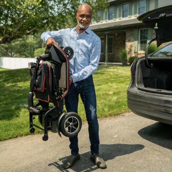 Man Holding The Feather Mobility Scooter In Front Of An Open Car Trunk Outdoors Man Holding The Feather Mobility Scooter In Front Of An Open Car Trunk Outdoors