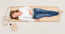 Overhead View Of A Smiling Woman Lying On The Cellvital Homecare CV-HC PEMF Therapy System Mat On A Carpeted Floor With The Control Unit Attached