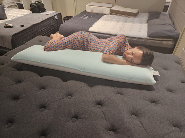 Overhead View Of A Woman Wearing A Dress Lying On The Standard Body Eurolux Green Planet Pillow Shown In A Showroom Setting