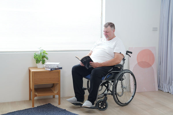 Patient Reading A Book While Sitting In A Wheelchair Using The Wellell Sedens 500 Seat Cushion With Battery Power Shown In A Hospital Setting
