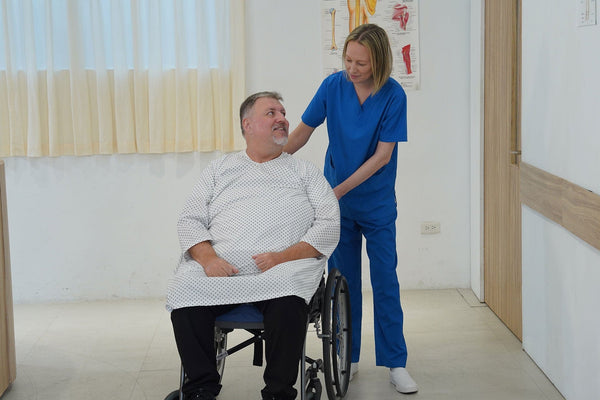 Patient Sitting On The Wellell Sedens 500 Seat Cushion With Battery Power While A Healthcare Worker Pushes His Wheelchair In A Hospital Setting