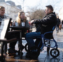 People Sitting At An Outdoor Cafe With A Person Using The Strongback Mobility SEATA Rollator