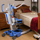 Rear Right Side View Of The Joerns Hoyer Journey® Sit To Stand Mobile Patient Lift Shown Beside A Bed In A Bedroom Setting