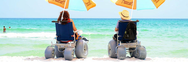 Rear View Of The Debug Mobility All-Terrain Beach Wheelchair Shown With Two Wheelchairs And Two People Looking Out At The Ocean In The Background