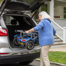 Rear View Of The Journey So Lite Mobility Scooter Shown In Blue Color With Elderly Woman Lifting The Scooter  Into The Trunk Of Her Car