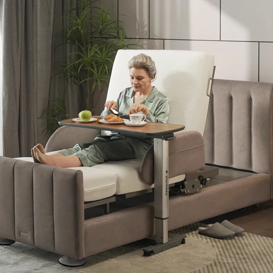 Right Side View Of A Woman Using The StarSleep Overbed Table For Drinking And Eating While Sitting On The StarSleep Arlo Rotating Bed Shown In A Bedroom Setting